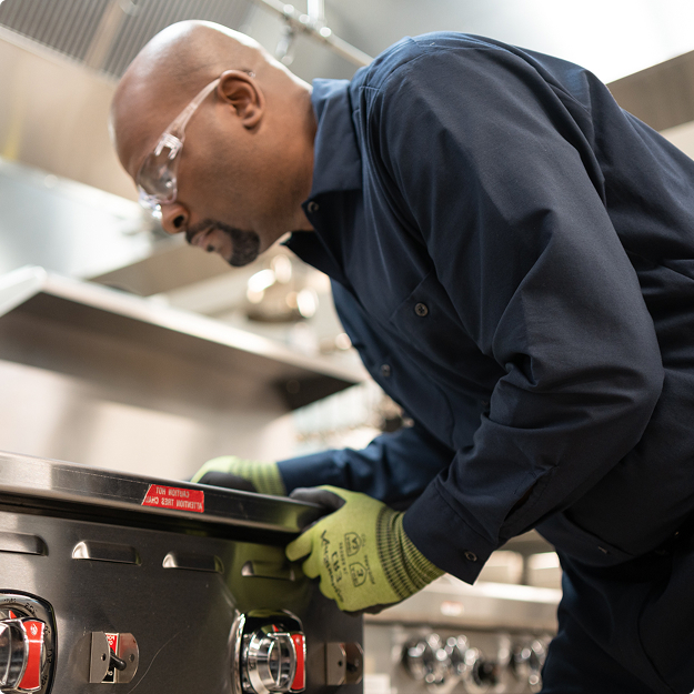 Technician in safety glasses and work gloves inspecting a commercial range