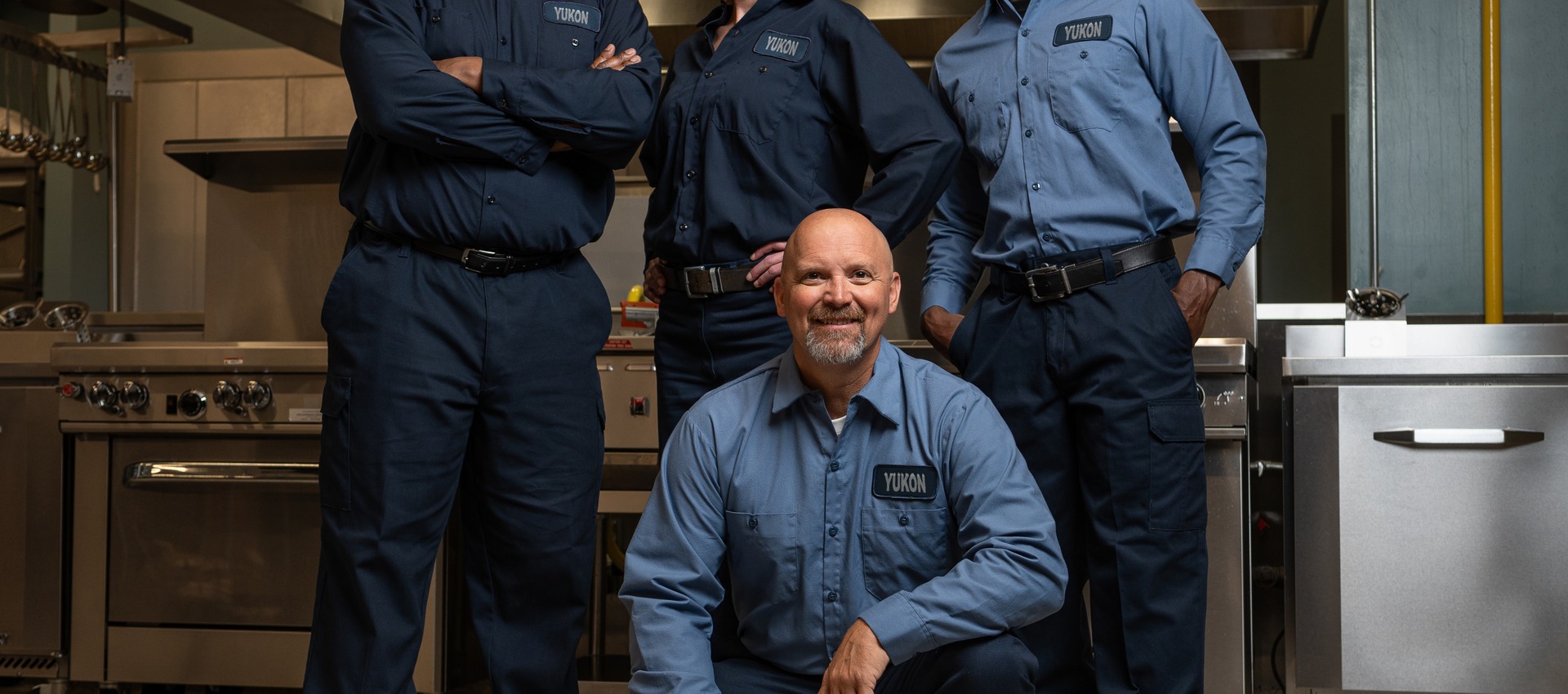Service team of four technicians in uniform posing in a commercial kitchen