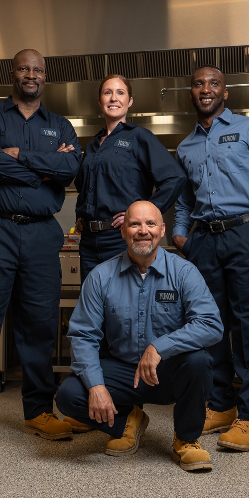Service team of four technicians in uniform posing in a commercial kitchen