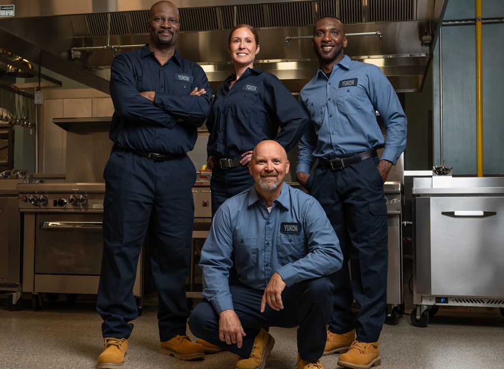 Service team of four technicians in uniform posing in a commercial kitchen