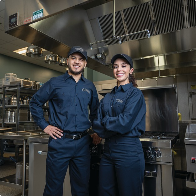 Two smiling technicians in uniform standing in a commercial kitchen
