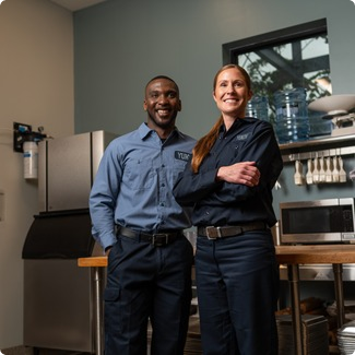 Two smiling technicians in uniform standing together in a commercial kitchen