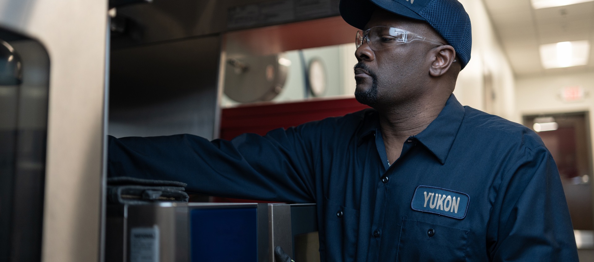 Yukon Refrigeration technician in a cap and safety glasses servicing commercial kitchen equipment