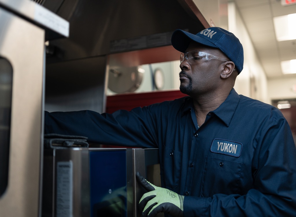 Yukon Refrigeration technician in a cap and safety glasses servicing commercial kitchen equipment