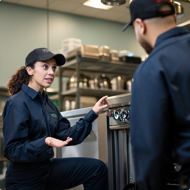 Technician in uniform explaining commercial kitchen equipment to a coworker during training