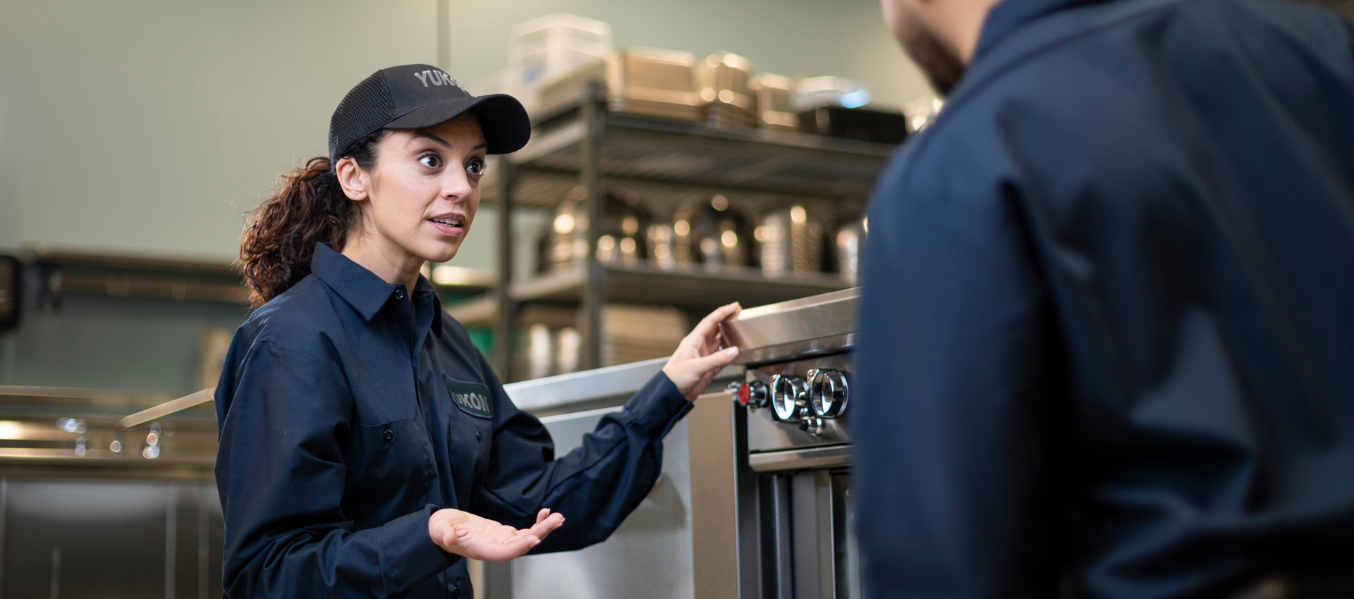 Technician in uniform explaining commercial kitchen equipment to a coworker during training