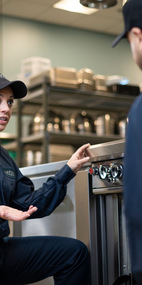 Technician in uniform explaining commercial kitchen equipment to a coworker during training