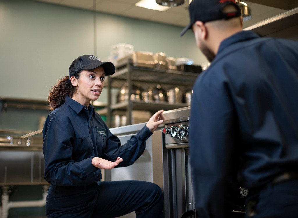 Technician in uniform explaining commercial kitchen equipment to a coworker during training