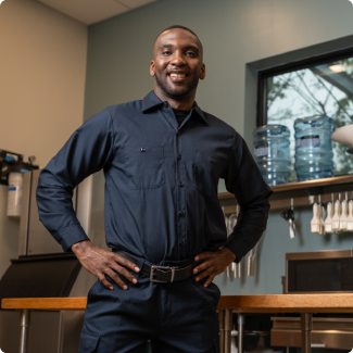 Smiling technician in a navy uniform standing with hands on hips in a commercial kitchen