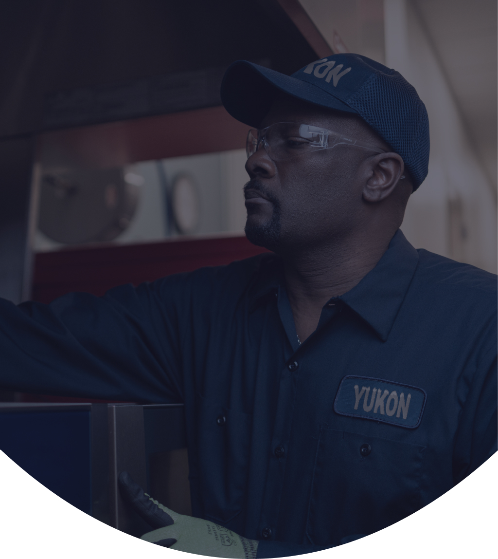 Yukon Refrigeration technician in a cap and safety glasses servicing commercial kitchen equipment