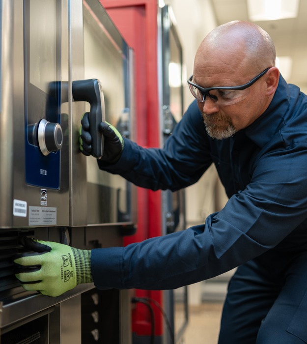 Technician in safety glasses and work gloves opening the door of a commercial combi oven